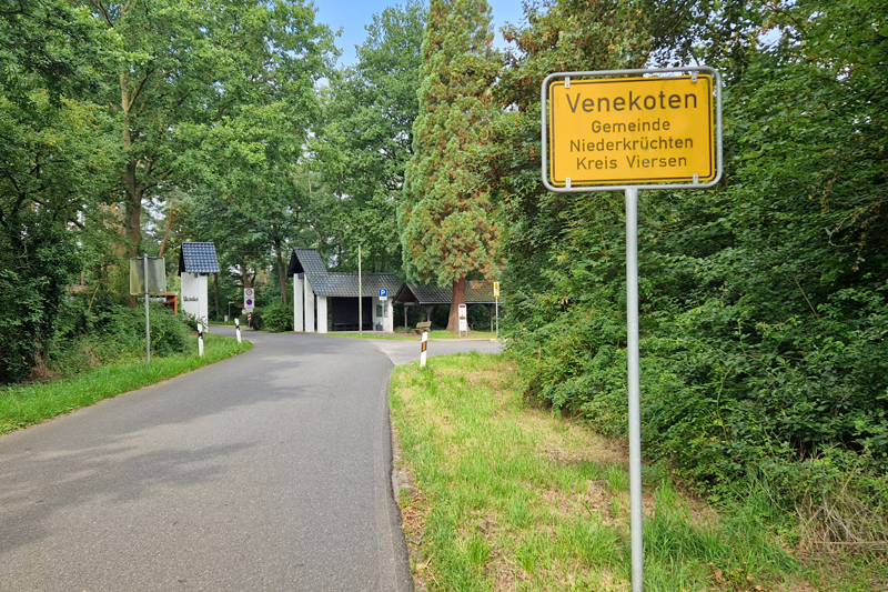 Ortseingang des Ortsteils Venekoten in der Gemeinde Niederkrüchten. Im Vordergrund das Ortseingangsschild mit der Beschriftung "Venekoten - Gemeinde Niederkrüchten - Kreis Viersen"