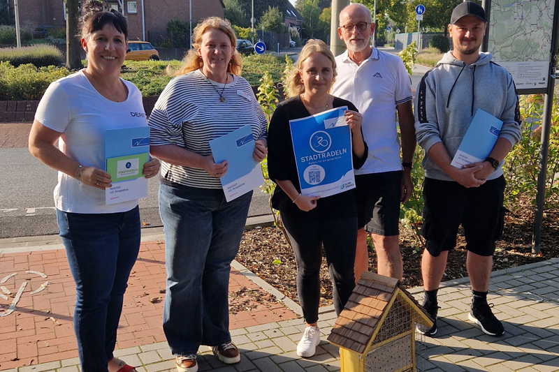 von links: Fritzi Brouwers, Ina Schmidt-Jansen, Lea Korall, Herbert von Seezen, Tobias Haese mit den Gewinnerurkunden Stadtradeln 2024. Im Hintergrund ein rot-weißes Verkehrsschild für Fahrradfahrer.