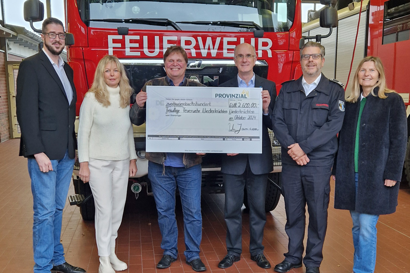 Vor einem Feuerwehrfahrzeug stehen von links: Erik Nagel, Maria van de Mortel, Ulrich Jansen (alle Provinzial), Hermann-Josef Schippers (Allgemeiner Vertreters des Bürgermeisters der Gemeinde Niederkrüchten), André Erkens (Leiter Freiwillige Feuerwehr) und Ilka Barth (Provinzial). Ulrich Jansen übergibt einen großen symbolischen Scheck an Hermann-Josef Schippers.