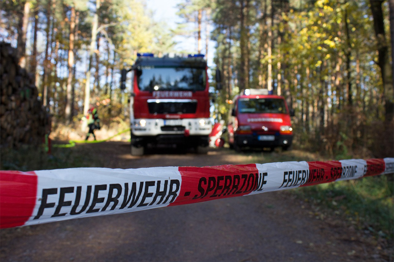 Zwei Feuerwehrwagen hinter Absperrband im Wald (Symbolbild)