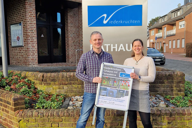 Frank Grusen und Svenja Sonnemans mit dem Plakat zur Veranstaltung "Niederkrüchten - Zuhause mit Perspektive" vor dem Rathaus der Gemeinde Niederkrüchten in Elmpt