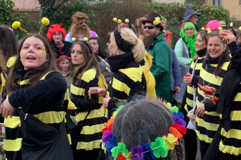 Teilnehmende des Tulpensonntagszugs in Niederkrüchten. Einige als Bienen verkleidet. Im Vordergrund ein Kopf mit Blumenkette von hinten.