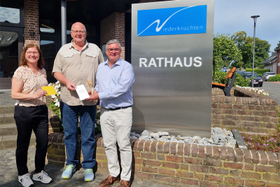 Beate Dohmen (Personalrat), Richard Dohmen und Bürgermeister Karl-Heinz Wassong vor einem Metallschild mit dem Logo der Gemeinde Niederkrüchten und der Aufschrift "Rathaus".